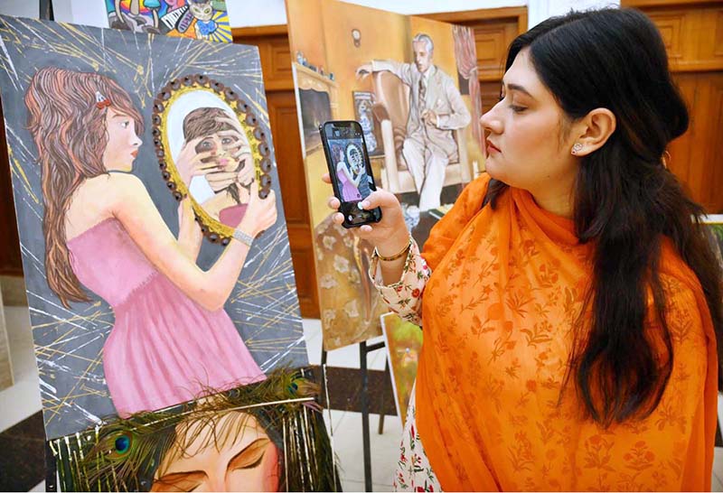 A visitor taking picture of display painting with her cell phone during celebration of International Day of Artists organized by Department of Social Welfare, Merged Districts in collaboration with Department of Art & Design UOP with the support of UNICEF